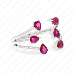 Peut inclure: Une bague ouverte argent&eacute;e orn&eacute;e de cinq pierres pr&eacute;cieuses rose vif en forme de poire, dispos&eacute;es dans un style bypass. L'anneau se divise en plusieurs branches en m&eacute;tal poli, chacune se terminant par une pierre en goutte d'eau.