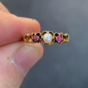 May include: A gold ring with a pearl and two ruby stones. The ring is set in a floral design.