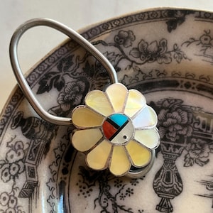 May include: A silver-toned metal key ring featuring a flower-shaped charm. The petals are made of iridescent cream-colored shell, while the center is inlaid with geometric segments of turquoise, red coral, black onyx, and white shell.