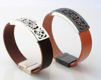 May include: Two leather bracelets with silver and black metal clasps. The clasps feature an intricate, cutout design.
