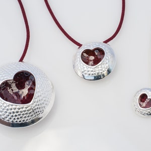 May include: Three silver necklaces with red heart pendants. The pendants are round and have a textured surface. The necklaces are of different lengths.