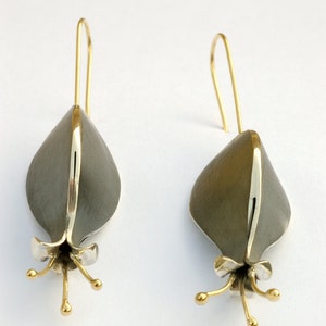 Puede incluir: Un par de pendientes de plata y oro en forma de flor con un acabado texturizado. Los pendientes tienen un dise&ntilde;o delicado y femenino.