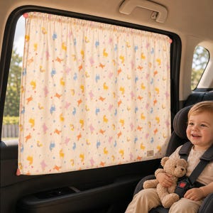 May include: A cream-colored car window curtain featuring a repeating pattern of small yellow, blue, and pink unicorns interspersed with tiny stars and triangles. The fabric is gathered at the top and attached to the interior frame of a vehicle window.