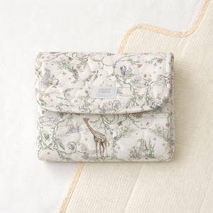 Könnte beinhalten: Eine gesteppte Stofftasche mit cremefarbenem Hintergrund und einem sich wiederholenden Muster aus grünen Ranken, kleinen Blumen und verschiedenen Tieren, darunter eine Giraffe, Kaninchen und ein Eichhörnchen. Ein kleines weißes Etikett zeigt mimi anunu.