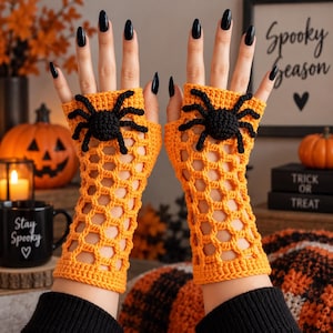 Puede incluir: Un par de guantes sin dedos de color naranja con un patrón de red de ganchillo y una gran aplicación de araña negra en el dorso de cada mano. Los guantes se extienden desde los nudillos hasta el antebrazo con un borde acanalado.