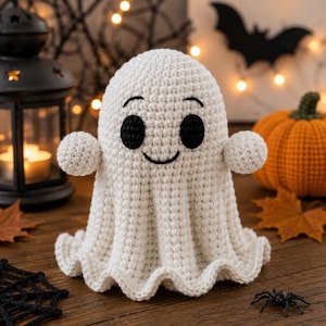 Puede incluir: Una figura de fantasma tejida a ganchillo en color blanco con cabeza redondeada, dos brazos pequeños extendidos hacia los lados y una base acampanada. El fantasma tiene dos ojos circulares negros grandes y una boca negra bordada y curva.