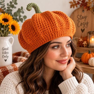 Peut inclure: Un béret au crochet orange vif en forme de citrouille, doté d'un motif côtelé texturé et d'une petite tige crochetée vert clair au centre. Le chapeau est réalisé avec un fil épais, créant une silhouette arrondie et volumineuse.