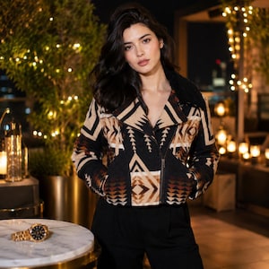 May include: A cropped jacket featuring a black, tan, and brown geometric pattern with a wide collar and a diagonal front zipper closure. The jacket is worn with solid black trousers, creating a structured look with long sleeves and a fitted waist.