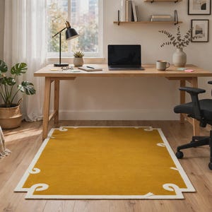 Handgetuft mosterdgeel vloerkleed met crèmekleurige lintrand, minimalistisch wollen tapijt met golvend krulmotief.