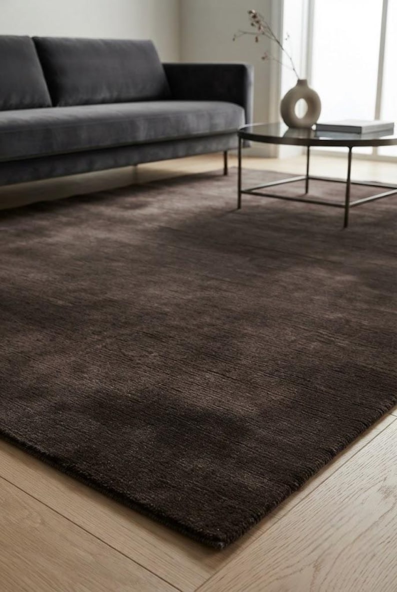 May include: A large, rectangular area rug in a deep, solid dark brown color. The rug features a dense, low-pile texture with subtle horizontal striations across its surface, providing a uniform appearance that covers the floor space.