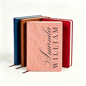 May include: Four rectangular journals with textured covers in blue, brown, pink, and red. The front pink journal features the black printed text Amanda WILLIAM in a combination of script and serif fonts, with each journal including a ribbon bookmark.