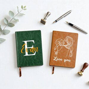 Puede incluir: Dos diarios rectangulares con cubiertas texturizadas. El diario verde presenta una letra E grande en blanco con el nombre Evan en cursiva amarilla. El diario marrón muestra una ilustración de línea blanca de una persona con un perro y el texto Love you.