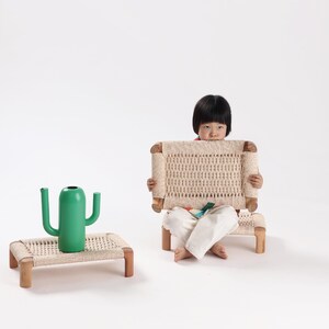 May include: Two low rectangular stools with light brown wooden frames and woven beige seats, accompanied by a bright green cactus-shaped watering can. The stools feature a simple four-legged design with a textured, woven surface pattern.