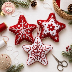 May include: Three star-shaped felt ornaments featuring hand-stitched embroidery. Two ornaments are red with white snowflake and floral patterns, while one is white with red snowflake embroidery. Each has a hanging loop and blanket-stitched edges.