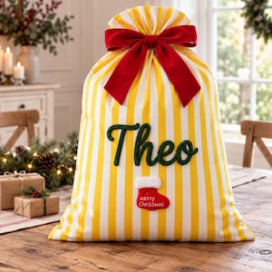 Può includere: Un sacco regalo a righe gialle e bianche con un grande fiocco in velluto rosso sulla parte superiore. Il nome Theo è ricamato in corsivo verde scuro e sotto è applicata una piccola toppa a forma di calza rossa con la scritta Merry Christmas.