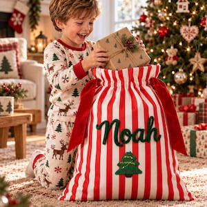 Può includere: Un grande sacco regalo in tessuto a righe verticali rosse e bianche, caratterizzato dal nome Noah in corsivo verde e da un'applicazione a forma di albero di Natale in feltro verde. Il sacco ha una chiusura a coulisse con nastri in velluto rosso.