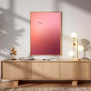 May include: A rectangular wall art print in a light wood frame featuring a vertical gradient that transitions from a soft pale pink at the top to a deep dark red at the bottom. The text "SO FAR SO GOOD" is printed in small black letters.
