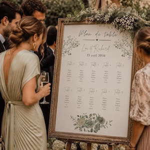 Peut inclure: Un plan de table de mariage dans un cadre doré orné sur un chevalet en bois. L'affiche porte l'inscription Plan de table, Lou et Richard, 15 avril 2034, et liste dix tables avec des noms. Elle est décorée d'illustrations botaniques vertes.