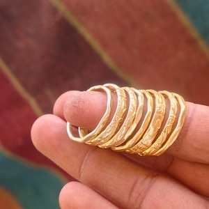 Peut inclure: Une pile de sept bagues fines en métal doré, chacune présentant un délicat motif floral gravé sur la bande extérieure. Les bagues sont uniformes en couleur et en design, avec une finition métallique polie qui reflète la lumière.