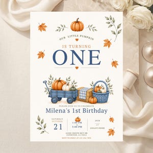 May include: A birthday invitation card featuring watercolor illustrations of pumpkins, autumn leaves, a blue wagon, and a blue basket. The text reads: Our little pumpkin is turning one, Milena's 1st Birthday, Saturday October 21, 1:00 PM to 3:00 PM, 2028 at Logan's home, 22500 Cristo Rey Dr, Cupertino, CA 95014, RSVP to Emily at 123-456-7890.