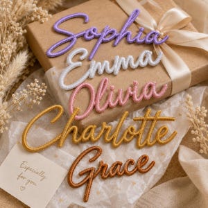 Op de afbeelding: Vijf geborduurde namen in cursief schrift met paarse, witte, roze, gouden en bruine draad. De namen Sophia, Emma, Olivia, Charlotte en Grace liggen op een bruine geschenkdoos met een crèmekleurig lint en een kaartje met de tekst Especially for you.