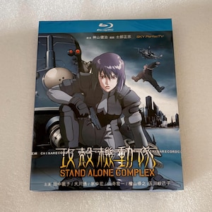 May include: A Blu-ray disc case for Ghost in the Shell: Stand Alone Complex featuring a central female character in dark tactical gear, a large mechanical vehicle, a helicopter, and a city skyline. The cover includes Japanese text and the title.