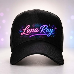 Könnte beinhalten: Eine schwarze Baseballkappe mit einer Neon-Grafik auf der Vorderseite. Der Schriftzug Luna Ray ist in einer stilisierten Schreibschrift in rosa und blauen Farbverläufen gehalten, umgeben von kleinen Sternen und Noten auf gepunktetem Grund.