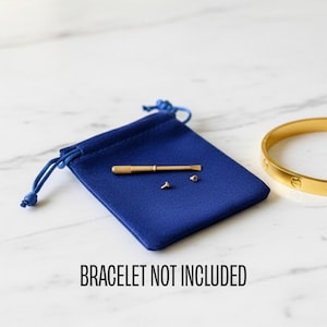 Könnte beinhalten: Ein goldfarbenes Armband mit einem Schraubendreher und kleinen Schrauben, präsentiert mit einem blauen Samtbeutel. Der Text "BRACELET NOT INCLUDED" ist darunter.