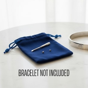 May include: A navy blue velvet pouch with a silver tool and two small screws. A silver bracelet is visible in the background. The text "BRACELET NOT INCLUDED" is printed in black.