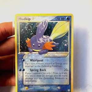 May include: A Mudkip Gold Star Pokémon trading card with 70 HP, featuring a holographic illustration of the blue creature. The card text includes the attacks Whirlpool and Spring Back, along with the rule: You can't have more than 1 Pokémon Star in your deck.