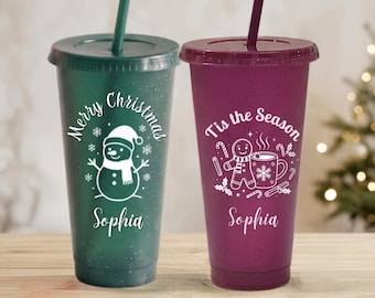 Puede incluir: Dos vasos de plástico con purpurina, tapas y pajitas. El vaso verde oscuro tiene un muñeco de nieve blanco, el texto Merry Christmas y el nombre Sophia. El vaso rojo oscuro tiene un hombre de jengibre, una taza, el texto Tis the Season y el nombre Sophia.