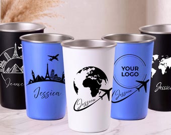 Puede incluir: Una colección de cinco vasos de acero inoxidable en negro, blanco y azul. Cada vaso presenta gráficos con temática de viajes, incluyendo mapas mundiales, horizontes urbanos, aviones y el nombre Jessica. Un vaso muestra el texto YOUR LOGO.
