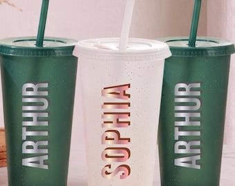 Puede incluir: Tres vasos de plástico reutilizables con tapas y pajitas. Dos vasos de color verde oscuro llevan el nombre ARTHUR en letras plateadas, mientras que el vaso blanco central lleva el nombre SOPHIA en letras oro rosa. Acabado moteado.