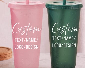 Puede incluir: Dos vasos de plástico reutilizables con tapa y pajita, uno rosa claro y otro verde oscuro. Ambos tienen un acabado moteado y texto blanco que dice Custom TEXT/NAME/LOGO/DESIGN. Los vasos tienen una forma cilíndrica recta.