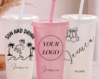 Puede incluir: Tres vasos de plástico con tapas y pajitas. Dos son blancos translúcidos con purpurina, uno es rosa sólido. El vaso izquierdo muestra un flamenco, palmeras y el texto "SUN AND DRINK". El vaso central dice "YOUR LOGO". El vaso derecho muestra cerezas.