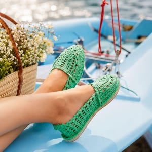 Op de afbeelding: Een paar felgroene gehaakte instapschoenen met een ingewikkeld opengewerkt patroon over het hele bovenwerk. De schoenen hebben een ronde neus en een laag profiel, gemaakt met een getextureerde garen afwerking en een platte, dunne zool.