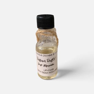 Puede incluir: Una pequeña botella de vidrio transparente llena de un líquido amarillo claro, con una tapa de rosca negra. Un trozo de cuerda está atado alrededor del cuello. La etiqueta dice Diffusor Duftöl, Duft: Hyazinthe y UFI-Code GEOY-58AH-X00U-PW9.