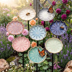 May include: A collection of eight ceramic flower-shaped dishes in various pastel colours, each mounted on a thin black metal stake. The dishes feature scalloped edges and a central floral pattern, with some occupied by live bees or monarch butterflies.