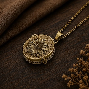May include: A round brass locket pendant on a matching chain, featuring a raised floral design on the front cover with intricate scrollwork detailing. The metal has a muted, aged finish, and the locket is attached to a simple link chain.