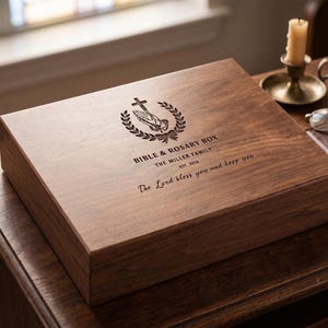 May include: A rectangular dark brown wooden box with a hinged lid featuring an engraved design of praying hands, a cross, and a laurel wreath. The text reads BIBLE & ROSARY BOX, THE MILLER FAMILY, EST. 2018, and The Lord bless you and keep you.