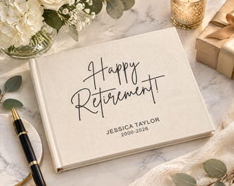 May include: A rectangular off-white fabric-covered guest book featuring the black printed text Happy Retirement! followed by the name JESSICA TAYLOR and the years 2000-2026. The book is positioned next to a black and gold ballpoint pen.