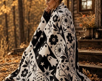 May include: A black and white throw blanket featuring a repeating pattern of ghosts, stars, flowers, and polka dots. The textile design incorporates botanical elements and celestial shapes arranged in a series of vertical panels across the fabric.