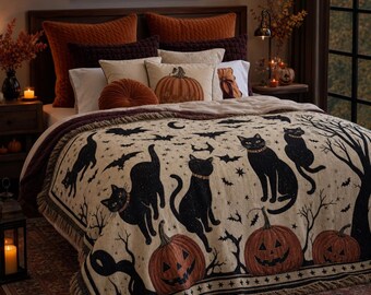 May include: A woven throw blanket featuring a cream background with a repeating pattern of black cats, orange jack-o'-lanterns, bats, and bare tree silhouettes. The blanket has a fringed edge and is draped over a bed with orange and brown pillows.