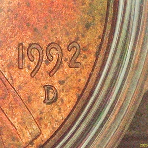 Peut inclure: Une vue rapprochée de la surface d'une pièce de monnaie couleur cuivre portant l'année 1992 et une marque d'atelier D estampillée dans le métal. La surface présente une patine texturée et usée avec des taches sombres et un bord en relief.