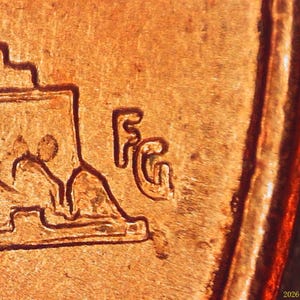 Può includere: Una superficie di moneta color rame che presenta una vista macro del design del rovescio del Lincoln Memorial. Le iniziali FG sono chiaramente impresse a destra della struttura del memoriale, con una texture metallica liscia e un bordo rialzato.