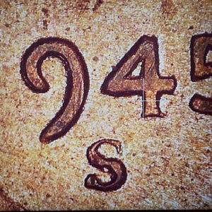 May include: A close-up view of a metallic surface featuring the embossed date 1945 and the mint mark S. The texture appears weathered with a copper-toned finish, showing raised numerals and a letter with dark, defined outlines against a grainy background.