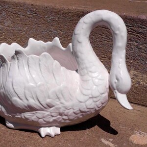 Peut inclure: Un cache-pot ou bol en céramique blanche en forme de cygne avec une finition brillante et des textures de plumes moulées détaillées sur le corps. Le cygne possède un long cou courbé et un bord festonné créant un bassin creux pour l'exposition.