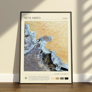 Op de afbeelding: Een ingelijste wandkunstprint met een satellietweergave van de regio Béni Abbès in Algerije. De afbeelding toont okerkleurige woestijnduinen, witte zoutvlaktes en donker terrein. De tekst bevat de plaatsnaam, coördinaten en beschrijvende details.