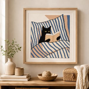 Puede incluir: Un bordado en punto de cruz enmarcado en forma cuadrada que muestra un gato negro con ojos amarillos leyendo un libro abierto. El gato está recostado sobre una almohada con rayas diagonales azules y blancas y un fondo color melocotón.