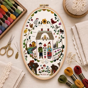 May include: An oval embroidery hoop containing a white fabric panel with a colorful needlepoint scene of a house, two figures, birds, flowers, and animals. The design includes the year 1991 at the bottom, surrounded by various embroidery floss skeins.